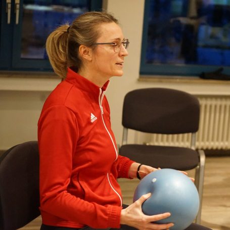 Ältere Frau streckt sich im sitzen.